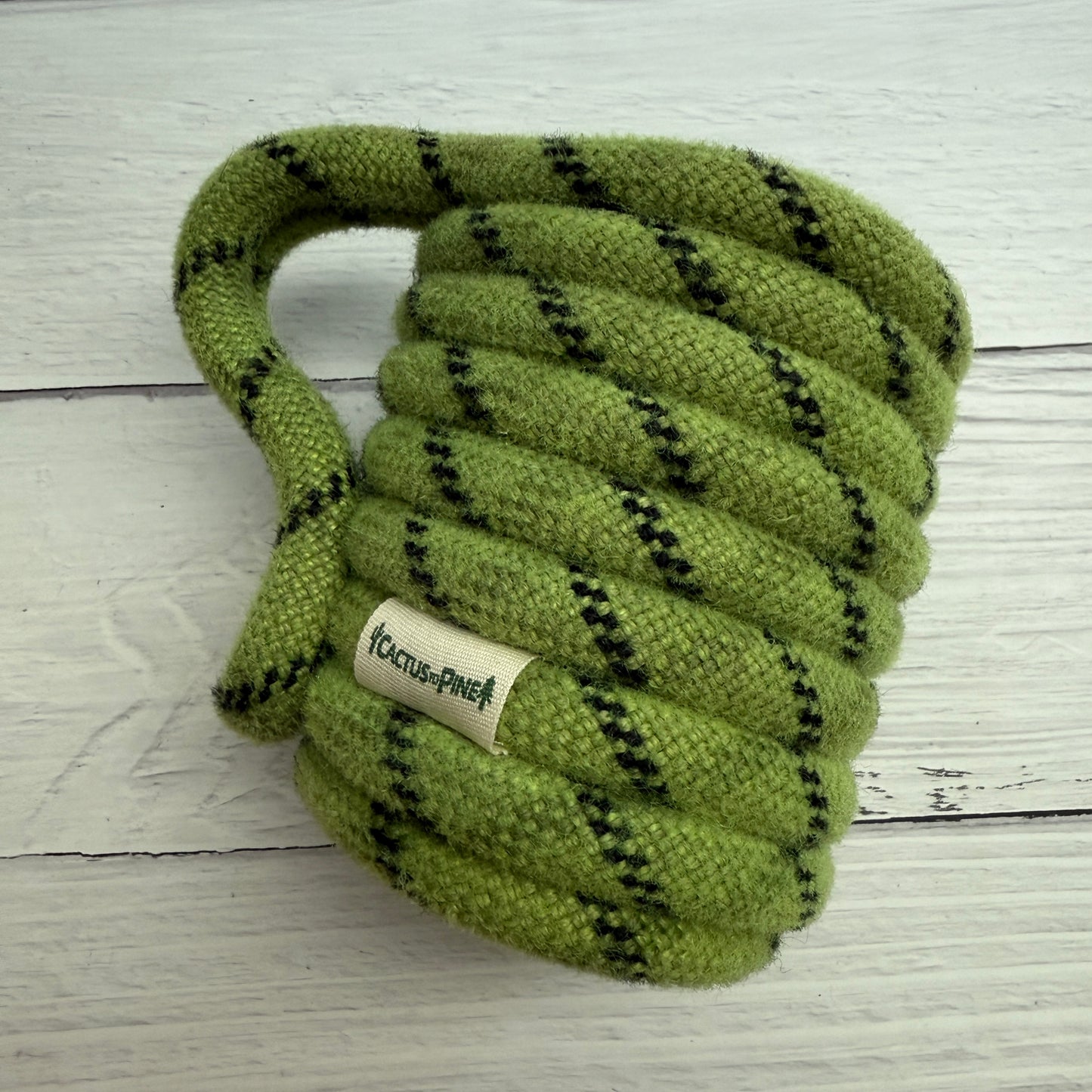 A green and black striped rope toy is placed on a white wooden surface.
