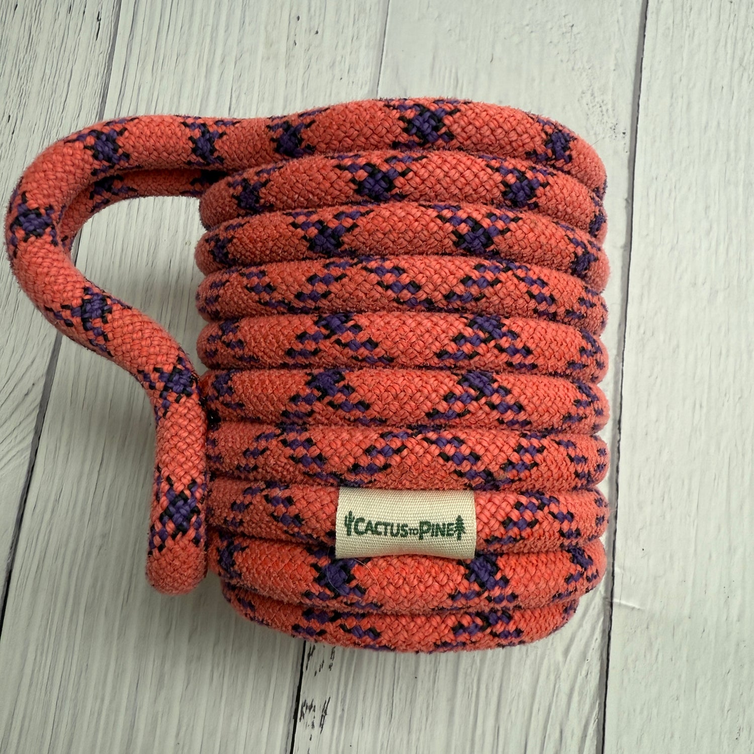 A coiled orange and purple rope with a label that reads "Cactus Pine" on it, resting on a white wooden surface.