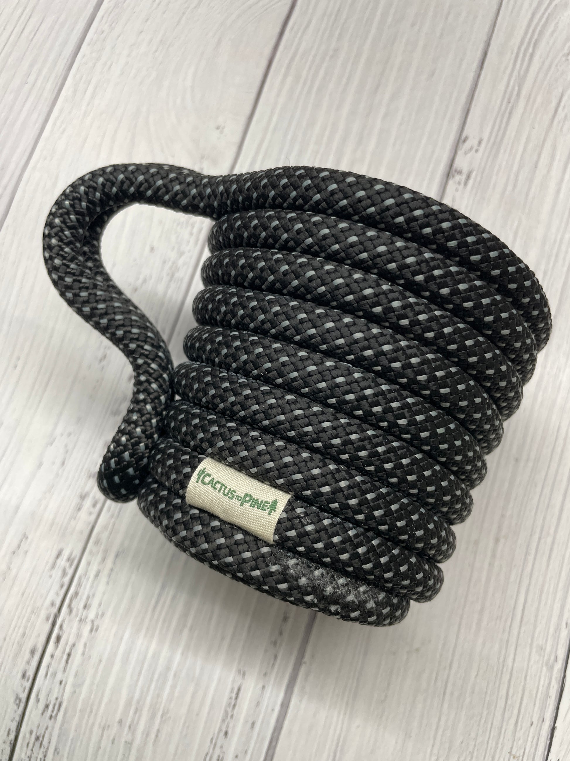 A black braided rope with a white label on it, resting on a white wooden surface.