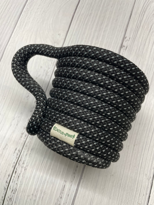 A black braided rope with a white label on it, resting on a white wooden surface.